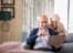 A man and a woman sitting on a couch looking at a laptop.