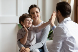 Overjoyed little boy giving a high five to male doctor at consultation at home with mom
