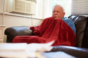  A Senior man trying to stay warm under a red blanket while sitting on the sofa.
