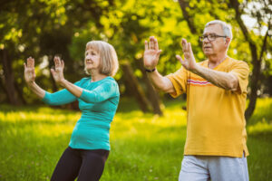 A senior couple with their hands facing outwards performing tai-chi movements in the park.
