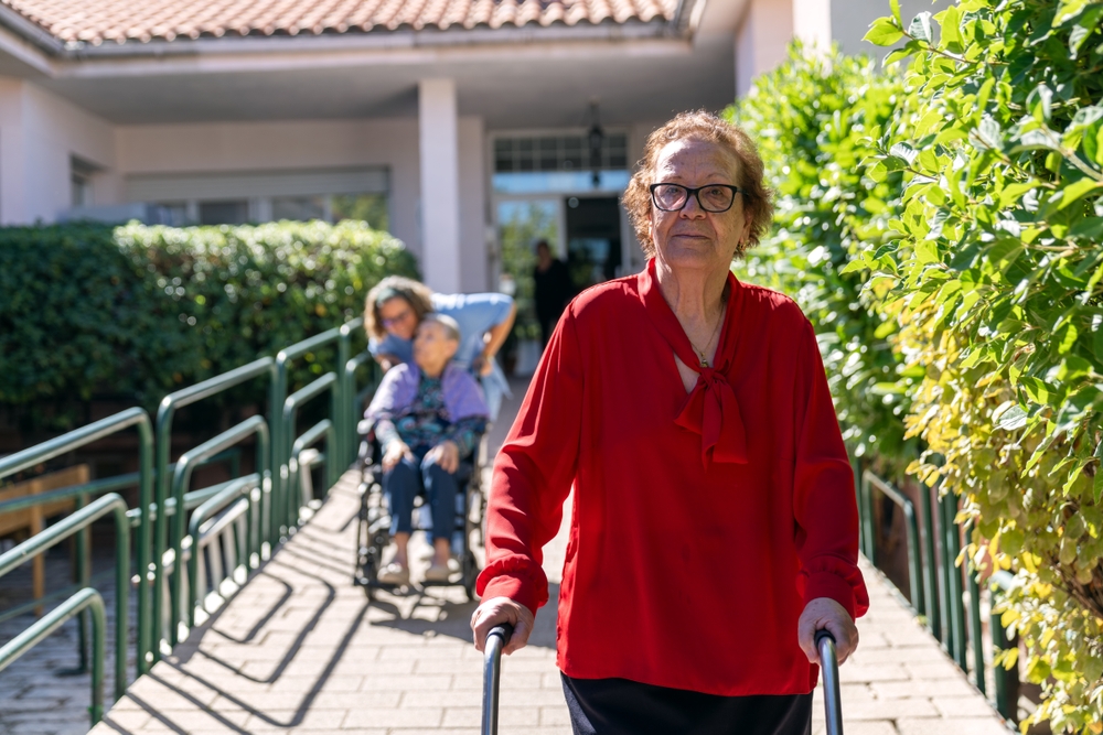 A woman wearing a red blouse descending a ramp while pushing her walker.
