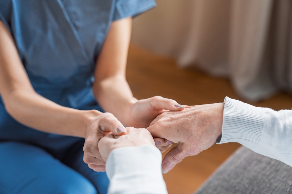 A homecare worker touching the arthritic hands of an elderly patient.