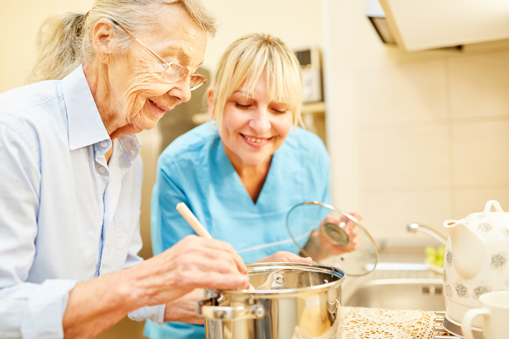 Caregiver helping a senior woman cook in the kitchen.